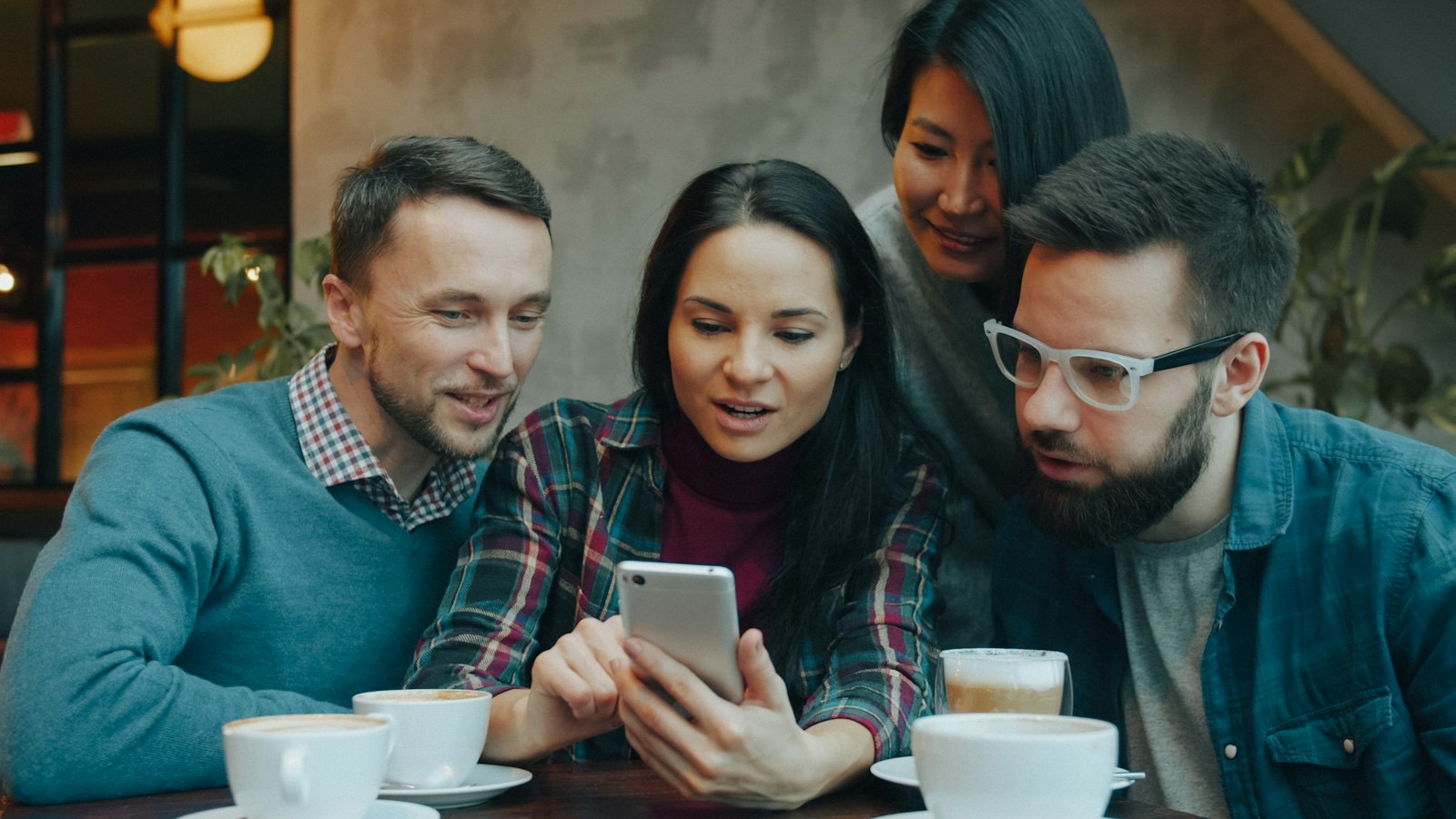 Quatre amis regardent un téléphone autour d'un café